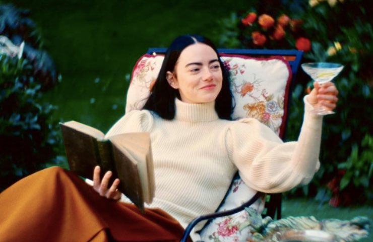 Emma Stone seduta in giardino sorride con un libro in mano 